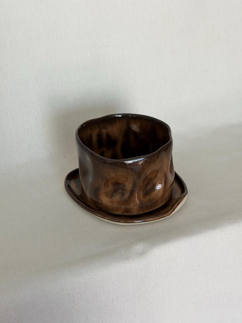 Mottled brown cup and saucer, a handbuilt ceramic cup pressed into dimples under a mottled brown glaze, 10 oz