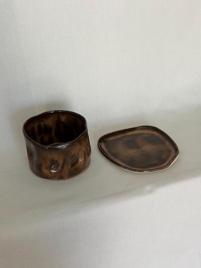 Mottled brown cup and saucer, a handbuilt ceramic cup pressed into dimples under a mottled brown glaze, 10 oz