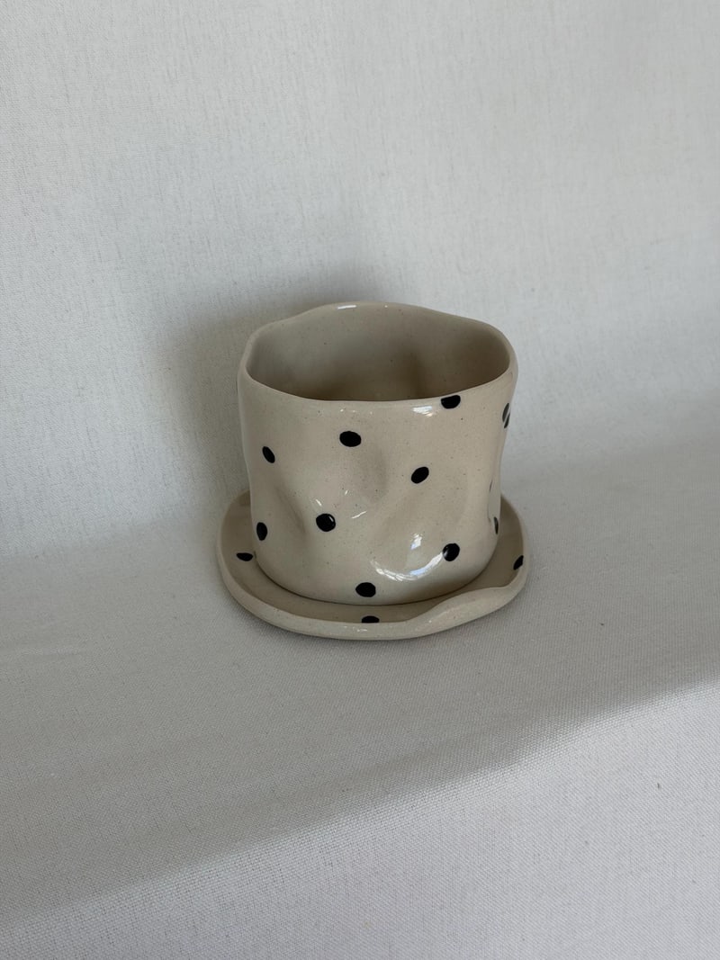 A handbuilt ceramic cup with black dots on a matching saucer, photographed in the Los Angeles studio